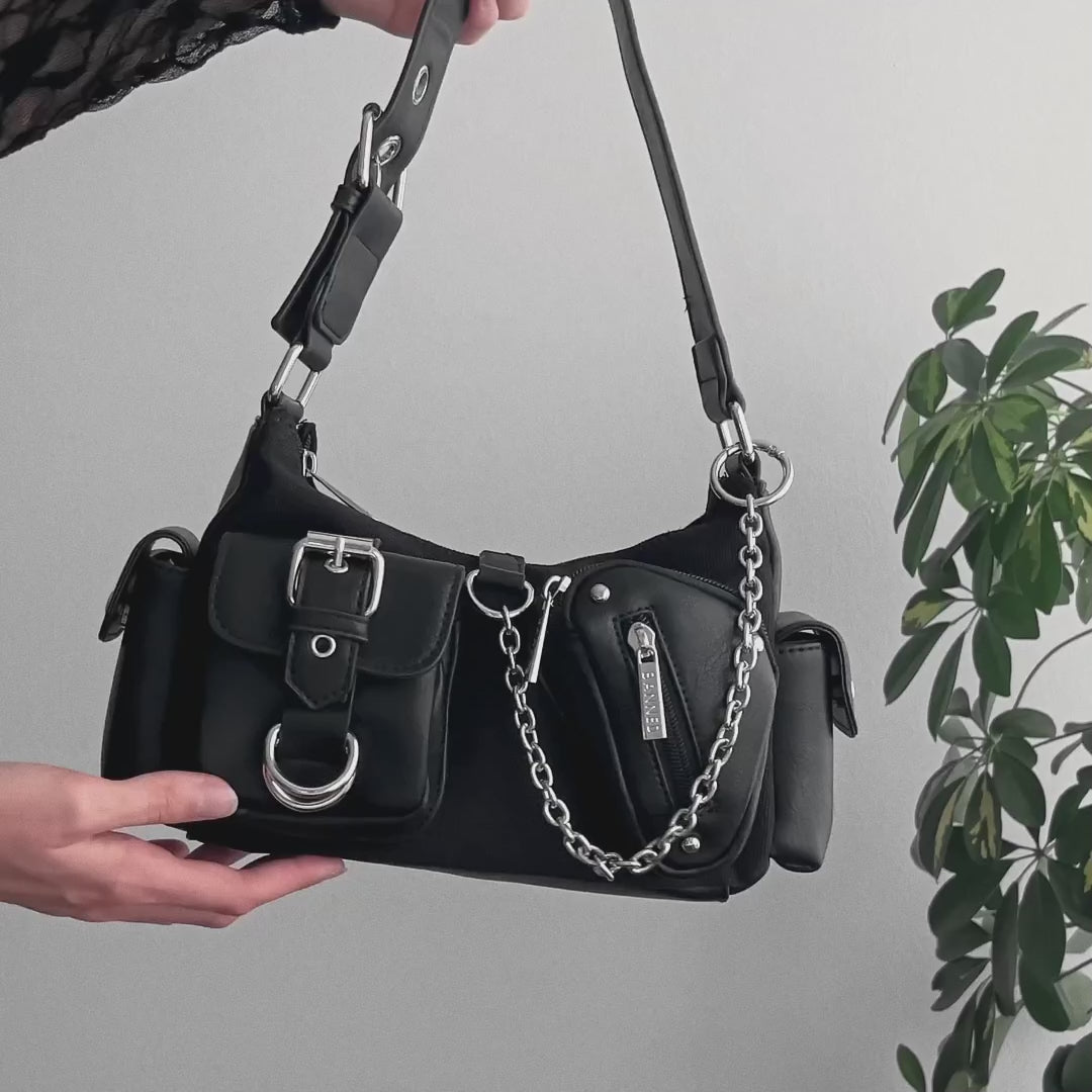 Video detalle de bolso baguette con múltiples bolsillos y detalles de remaches, hebillas y cadenas metálicas estilo y2k.