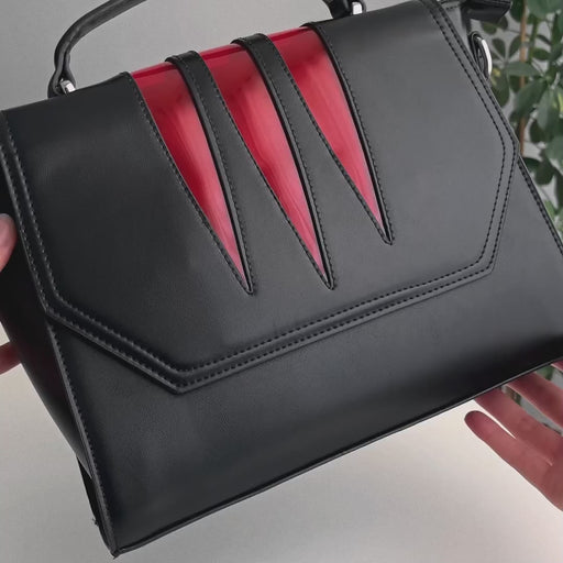 Video en detalle de bolso rígido rectangular con detalles en color rojo en la solapa estilo vamp goth.