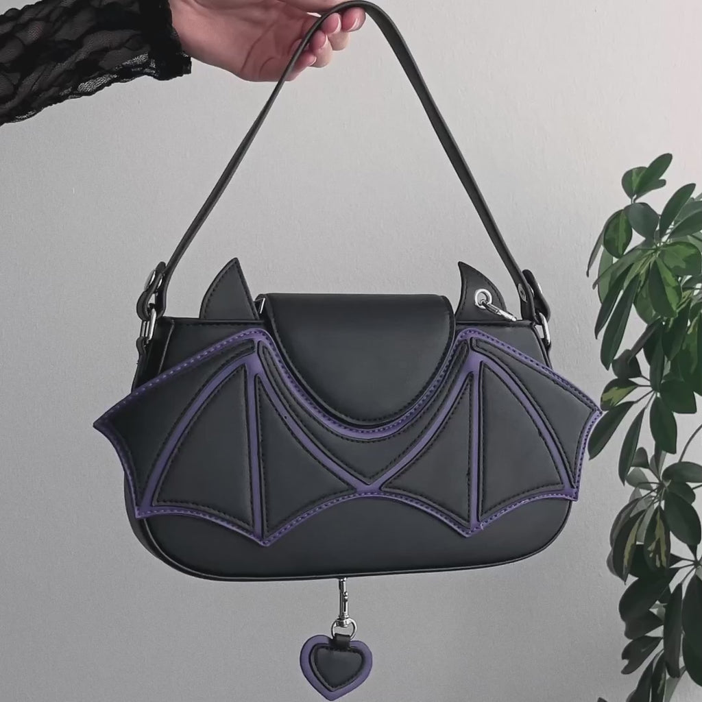 Video detalle de bolso de hombro baguette con apliques en forma de murciélago y detalles en color morado con charm en forma de corazón.