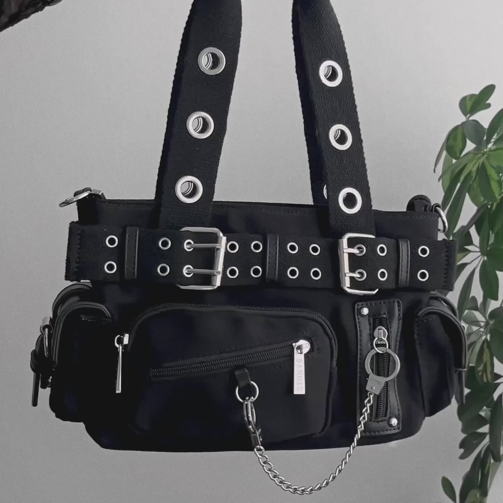 Video detalle de bolso baguette con múltiples bolsillos, remaches, hebillas y cadenas en forma de esposas estilo y2k. 