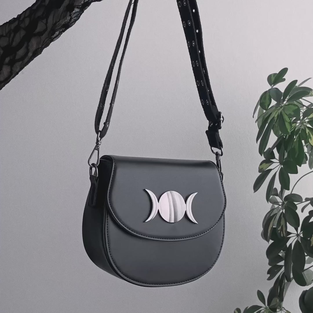 Video detalle de bolso saddle rígido pequeño con remaches en la correa y detalle metálico de triple luna en la solapa estilo witchy.