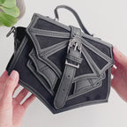 Bolso de mano pequeño estilo gótico con inspiración en los murciélagos sujetado por unas manos que enseñan sus detalles en el tejido y las hebillas metálicas