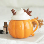 Quemador de aceites esenciales y calentador de cera con forma de taza de calabaza con nata montada encima estilo halloween otoñal vista frontal sobre escritorio con decoración al rededor.