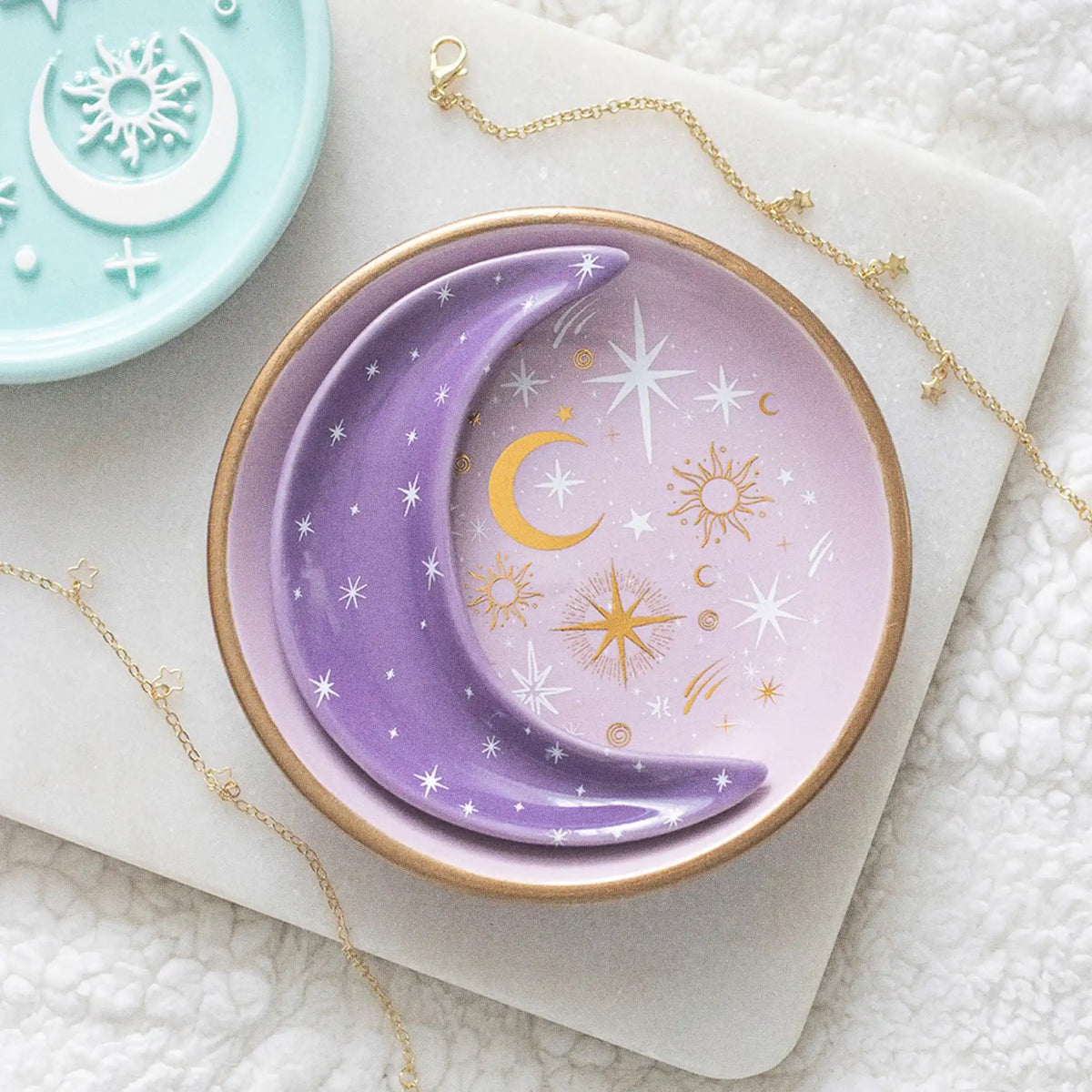 Set de dos platos joyeros apilables en forma de círculo y luna con motivos celestiales en tonos blancos y dorados vista desde arriba sobre escritorio con decoración al rededor.