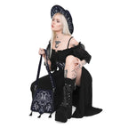 Bolso rígido en azul medianoche con ribetes en negro, bordado en tonos plateados con un diseño celestial de polilla, luna, estrellas y vegetación estilo whimsigoth. Borlas decorativas en la solapa. Vista con modelo agachada