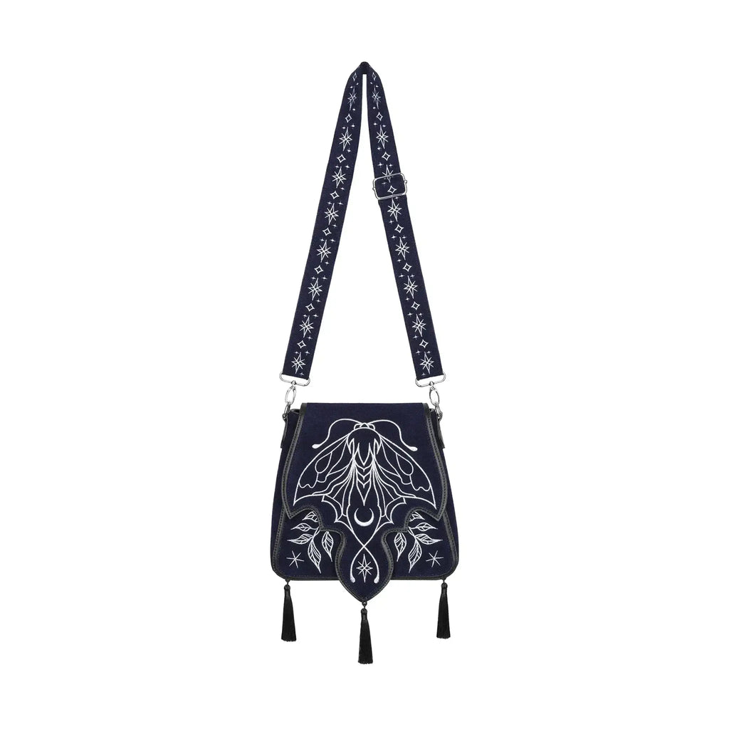 Bolso rígido en azul medianoche con ribetes en negro, bordado en tonos plateados con un diseño celestial de polilla, luna, estrellas y vegetación estilo whimsigoth. Borlas decorativas en la solapa. Vista frontal completa con correa