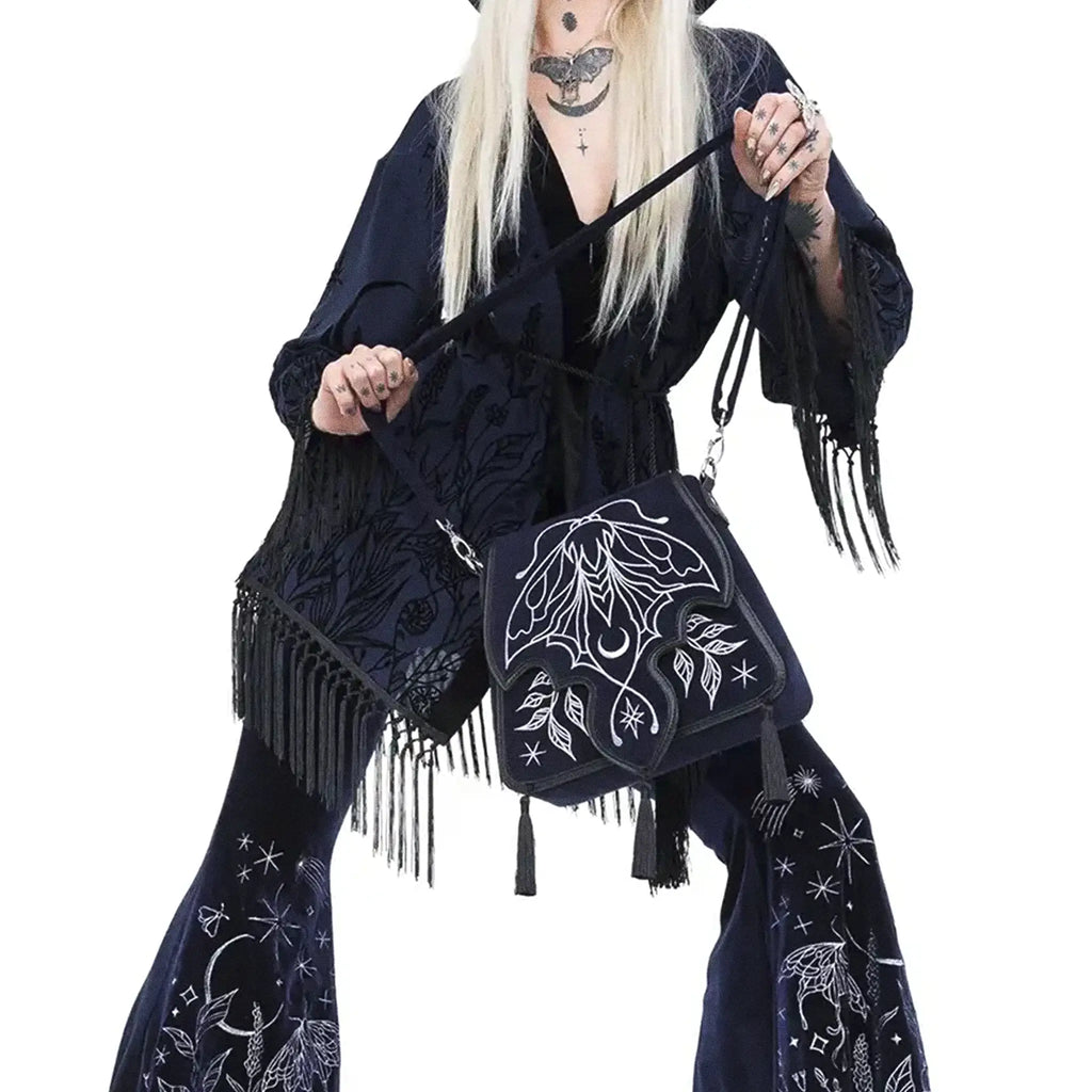 Bolso rígido en azul medianoche con ribetes en negro, bordado en tonos plateados con un diseño celestial de polilla, luna, estrellas y vegetación estilo whimsigoth. Borlas decorativas en la solapa. Vista con modelo