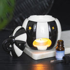 Quemador de aceites esenciales con forma de calabaza a rayas blancas y negras estilo gótico, witchy o alternativo vista posterior con vela encendida sobre escritorio con decoración al rededor.