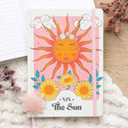 Libreta a5 de tapa dura con portada inspirada en el tarot apoyada sobre un escritorio con objetos decorativos al rededor.