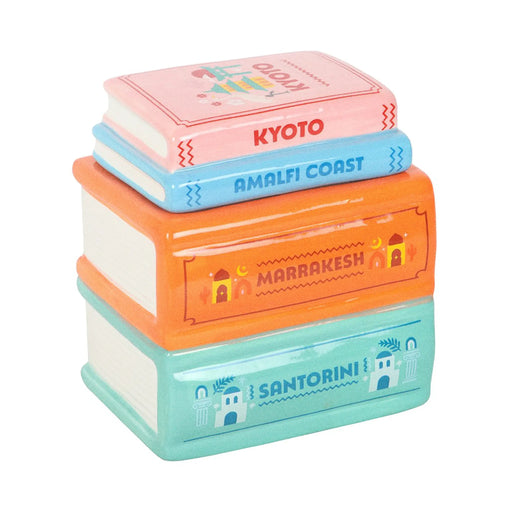 Quemador de aceites esenciales y calentador de cera en forma de libros apilados de diferentes destinos de viaje multicolor vista frontal sobre fondo blanco.