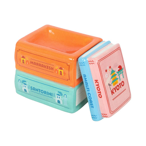 Quemador de aceites esenciales y calentador de cera en forma de libros apilados de diferentes destinos de viaje multicolor vista sin tapa sobre fondo blanco.