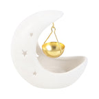 Quemador de aceites esenciales en forma de luna creciente en color blanco con estrellas cut out y recipiente colgante para aceites en color dorado vista frontal sobre fondo blanco.