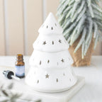 Quemador de aceites esenciales con forma de árbol de navidad y estrellas y gotas cut out en la superficie vista frontal sobre escritorio con decoración al rededor.